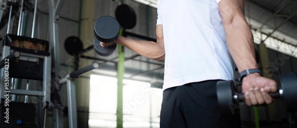 Fototapeta Focused Strength Training. Close-up of young man lifting dumbbells in gym.