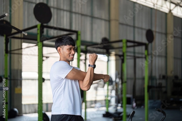 Fototapeta Strength and Flexibility. Young man stretching after workout in gym.