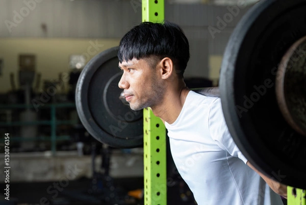 Fototapeta Strength Training. Man performing squat exercise with barbell in gym.