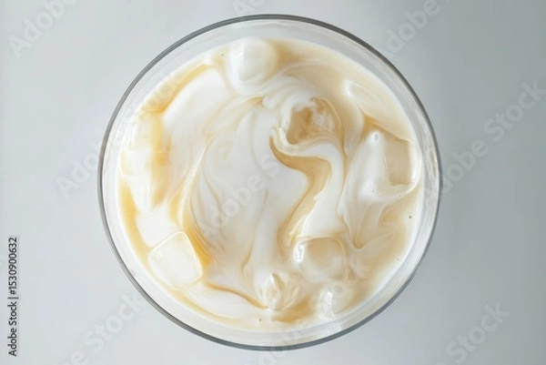 Fototapeta Top-down view of iced coffee with milk swirling in glass on a bright surface