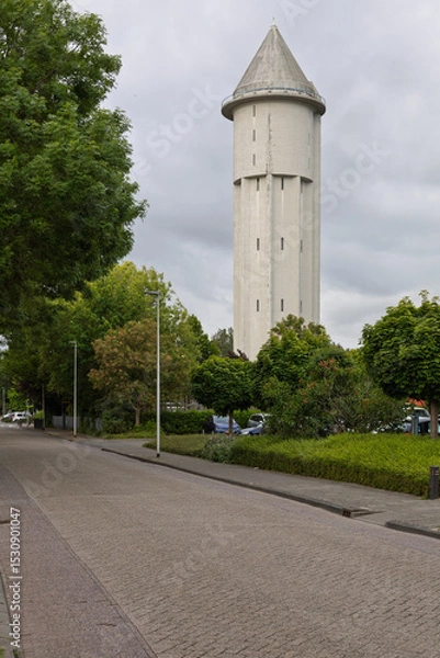 Obraz The iconic water tower of Meerkerk, Netherlands, stands tall under a cloudy sky, a distinctive landmark amidst green trees and a quiet street. Built in 1936.