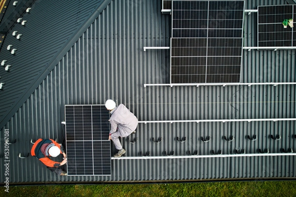 Fototapeta Mounters building photovoltaic solar module station on roof of house. Men electricians in helmets installing solar panel system outdoors. Concept of alternative and renewable energy. Aerial view.