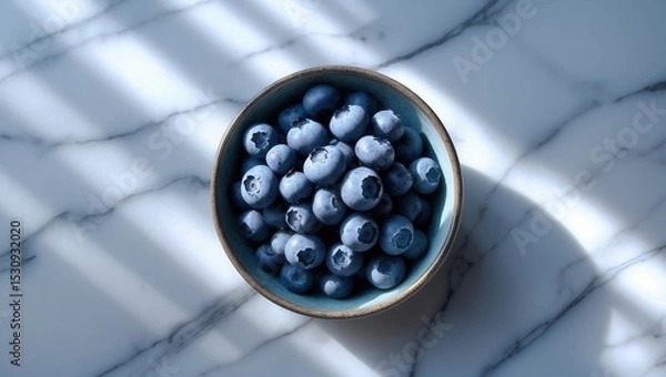 Fototapeta Bowl of fresh blueberries on a marble surface with soft sunlight and shadows