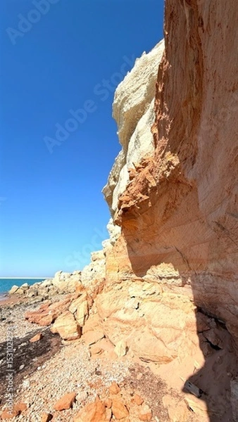 Fototapeta Colorful fossil rock formations rising on the seashore, creating dramatic contrast against clear blue sky, offering picturesque view of coastal geology