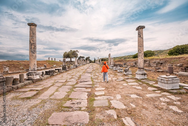Fototapeta Tourist walking through the ancient Roman road in Pergamon, Turkey, surrounded by ruins and columns, exploring the historical site