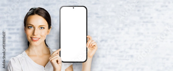 Fototapeta Portrait image - happy smile cute businesswoman business woman show point big mockup cell phone, smartphone mobile cellphone with white screen. Online offer ad. Free text space. Bricks wall background