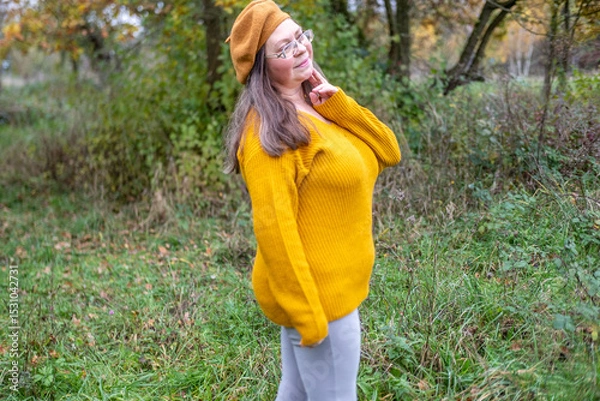 Obraz Happy middle-aged woman in mustard sweater and beret, enjoying autumn, smiling, joyful expression, outdoors, fall season, outdoor Mature portrait, forest background