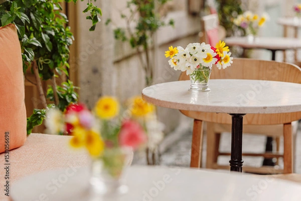 Fototapeta Small glass vase containing a colorful bouquet of wildflowers decorating a table in a restaurant with an out of focus background