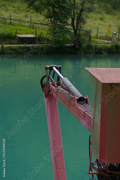 Fototapeta A robust hydraulic arm in bold red and silver stands against a calming teal backdrop, showcasing industrial power and precision
