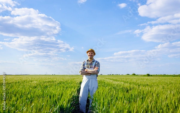 Obraz Portrait of adult male farmer standing in green wheat field looking at camera.