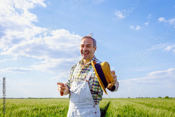 Obraz Portrait of joyful farmer standing in green wheat field looking at camera.