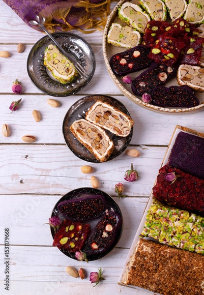 Fototapeta Sliced ​​Turkish delight assortment with cream filling, pistachio, almond, hazelnut, figs and cranberry laid out on plates on a white table. Local name: fistikli fitil lokum