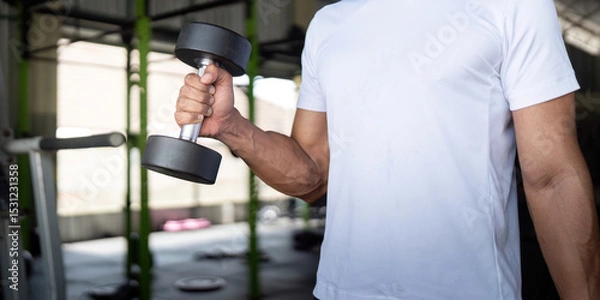 Fototapeta Focused Exercise. Young man lifting a dumbbell in gym for strength and fitness.