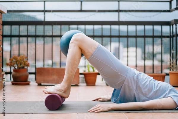 Fototapeta Woman doing glute bridge with foam roller and Pilates ball for hypermobility training