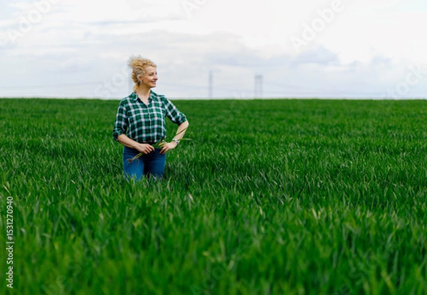 Obraz Portrait of adult female farmer standing in green wheat field.
