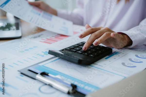 Obraz Businesswoman analyzing financial charts and using calculator in office