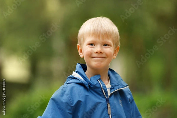 Obraz A portrait captures a charming young boy with bright blonde hair and a sweet, slightly mischievous smile. He is wearing a blue hooded jacket, suggesting he's enjoying time outdoors