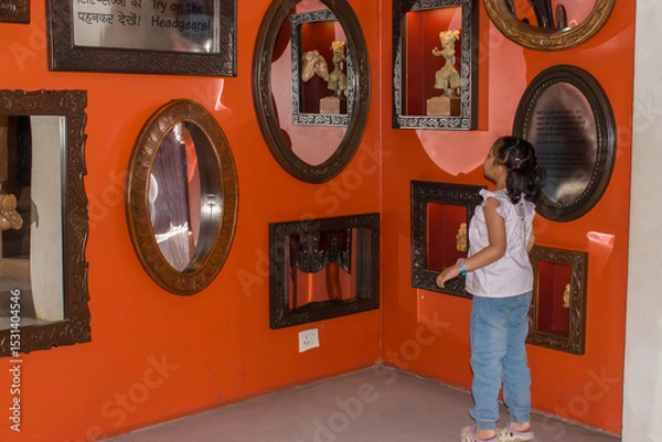Obraz Adorable little girl child on her tiptoes exploring the mirror section of a museum. She gazes curiously at her own reflection, filled with wonder and excitement. childhood curiosity, learning