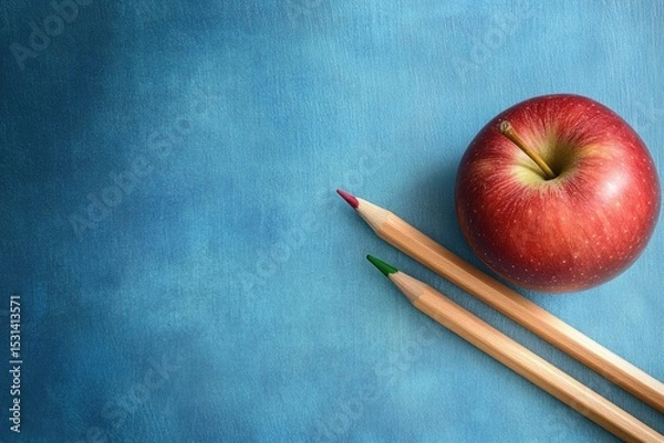 Fototapeta A red apple rests beside two colored pencils on a textured blue surface