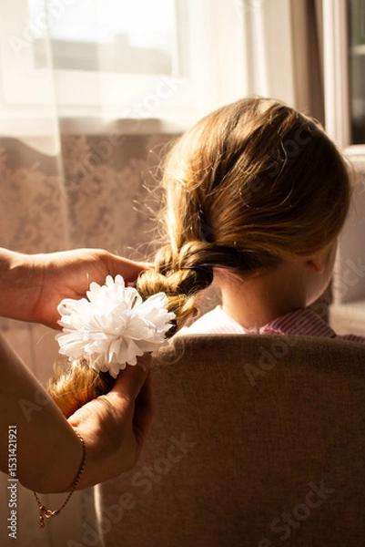 Fototapeta Close-up of mother hands weaving a delicate braid in her daughter's fine hair. Tender moment of feminine connection and care.