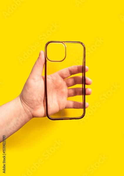 Fototapeta Hand holding a transparent smartphone case against a vibrant yellow background, showcasing modern design and functionality for mobile device protection and style enhancement
