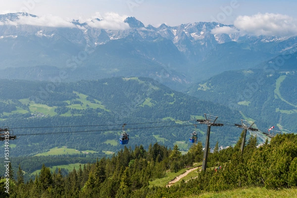 Fototapeta Hiking above the clouds on Wankberg, Germany—panoramic views of snow-capped Alps and lush valleys under a bright blue sky.