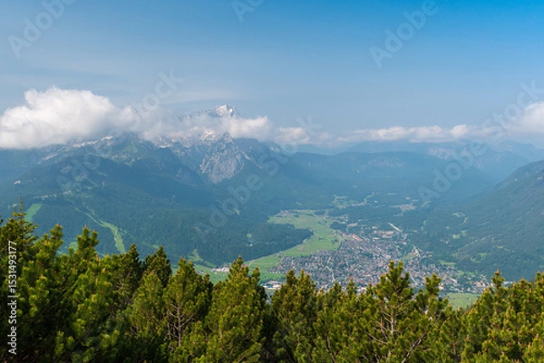 Fototapeta Hiking above the clouds on Wankberg, Germany—panoramic views of snow-capped Alps and lush valleys under a bright blue sky.