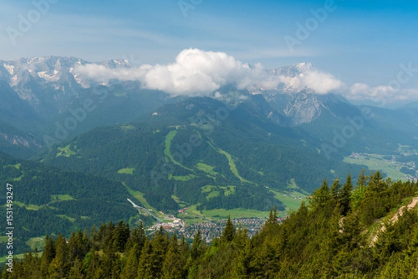 Fototapeta Hiking above the clouds on Wankberg, Germany—panoramic views of snow-capped Alps and lush valleys under a bright blue sky.