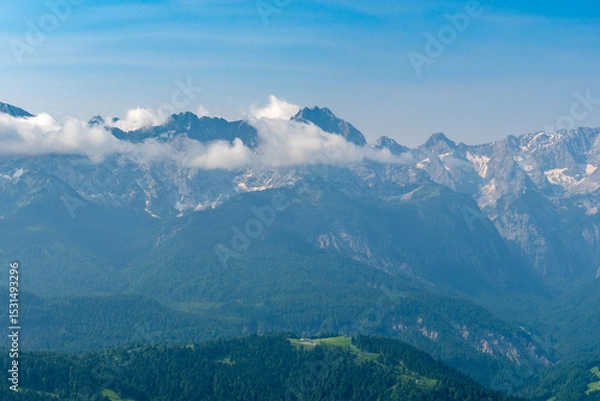 Fototapeta Hiking above the clouds on Wankberg, Germany—panoramic views of snow-capped Alps and lush valleys under a bright blue sky.