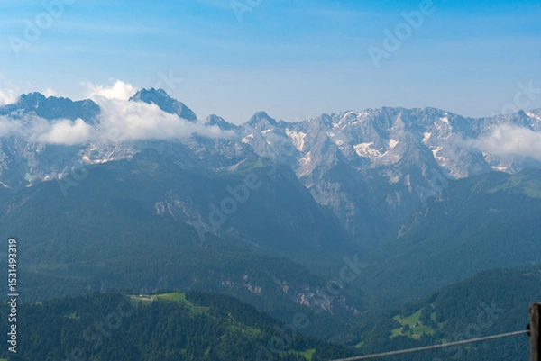 Fototapeta Hiking above the clouds on Wankberg, Germany—panoramic views of snow-capped Alps and lush valleys under a bright blue sky.