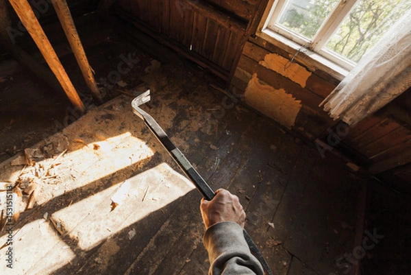 Obraz Person holding a crowbar in an old, derelict wooden room with sunlight