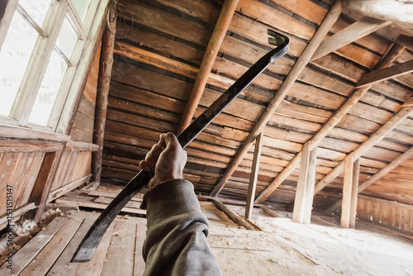 Obraz A person holding a crowbar inside an old wooden attic