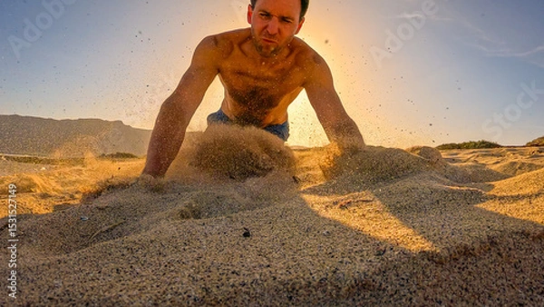 Fototapeta LOW ANGLE VIEW: Clumsy man stumbles and falls into sand while running beach in early morning. Sand flies in all directions in golden light while young man hits the sandy ground after spectacular fall.