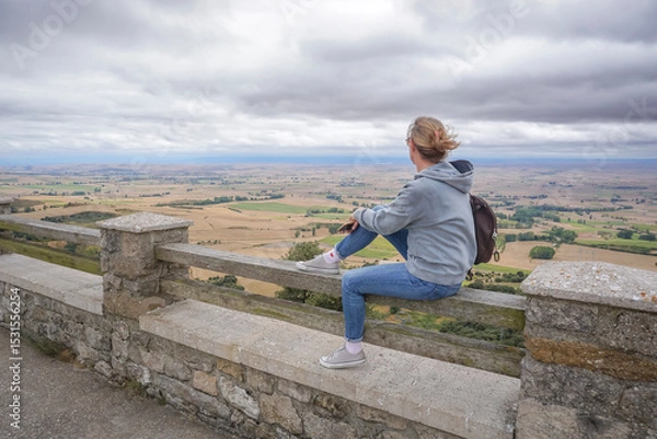 Obraz Young woman wearing jeans and a gray sweatshirt contemplating the landscape of the province of Burgos on a cloudy day from a viewpoint