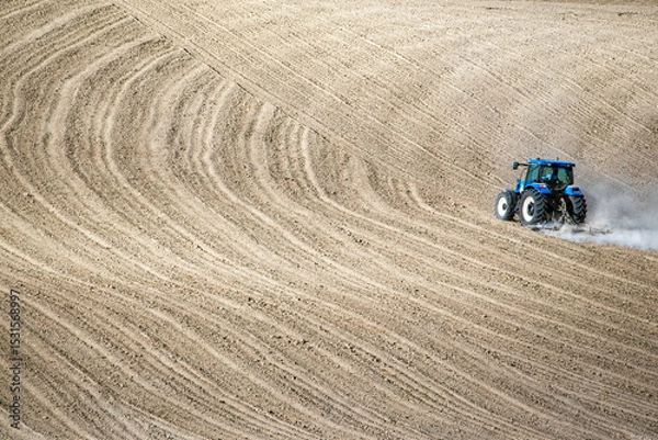 Fototapeta A tractor moves across freshly plowed wavy soil, highlighting agricultural machinery and rural productivity in a minimalist landscape.