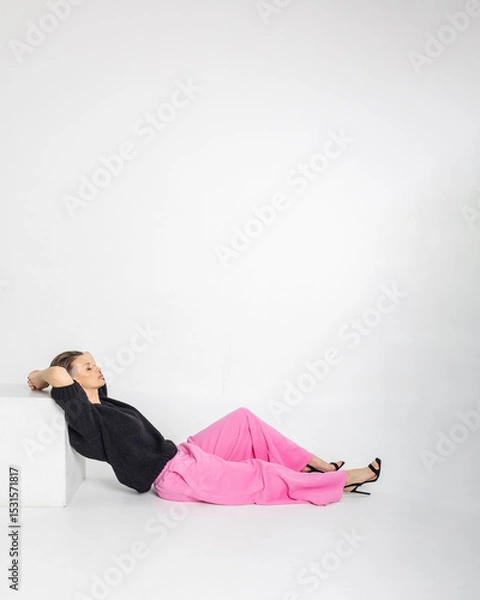 Obraz Portrait beautiful woman of model appearance. Girl in black jumper and pink trousers on grey background. Pretty female with trendy makeup posing in studio. Vertical photo. 