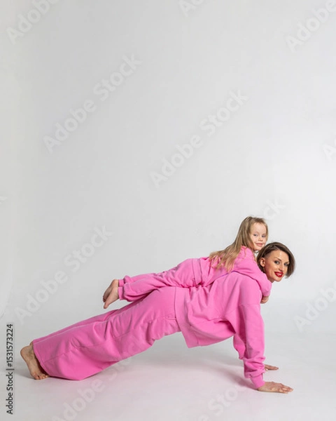 Obraz Young mother and little daughter walking holding hands. Dressed in pink color suits on white background, studio. Concept of advertising positive and clothes. Vertical photo