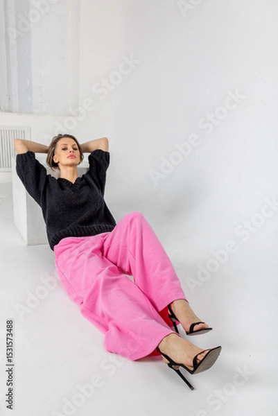 Obraz Portrait beautiful woman of model appearance. Girl in black jumper and pink trousers on grey background. Pretty female with trendy makeup posing in studio. Vertical photo. 
