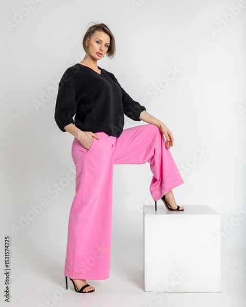 Obraz Portrait beautiful woman of model appearance. Girl in black jumper and pink trousers on grey background. Pretty female with trendy makeup posing in studio. Vertical photo. 