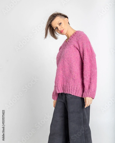 Obraz Portrait beautiful woman of model appearance. Girl in pink jumper, black trousers on grey background. Pretty female with trendy makeup posing in studio. Vertical photo.
