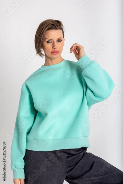 Obraz Portrait beautiful woman of model appearance. Girl in mint jumper, black trousers on grey background. Pretty female with trendy makeup posing in studio. Vertical photo.