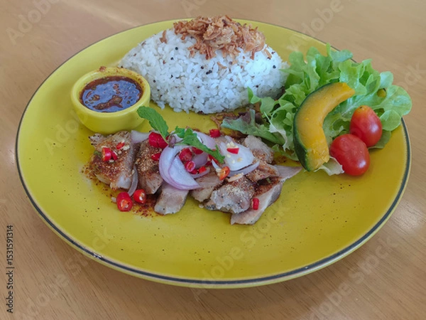 Fototapeta thai food, waterfall pork, fried garlic on rice and nam jim jaew in a yellow bowl, green vegetables, 1 piece of pumpkin, 2 tomatoes on a large yellow dish on a wooden background, food, copy space