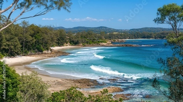 Fototapeta Coastal beach scene with turquoise water and sandy shore. Lush trees and hills in the background