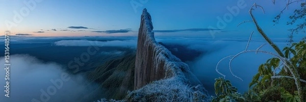 Fototapeta Majestic Panoramic View of Sharp Mountain Peak Surrounded by Clouds at Serene Blue Hour Twilight