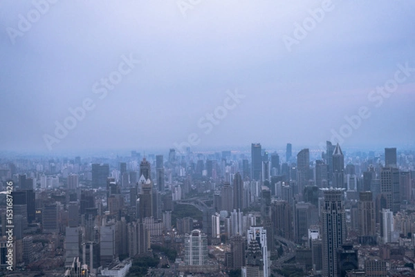 Fototapeta Aerial view of Shanghai city skyline under cloudy evening sky, showing dense high-rise buildings and sprawling urban layout.