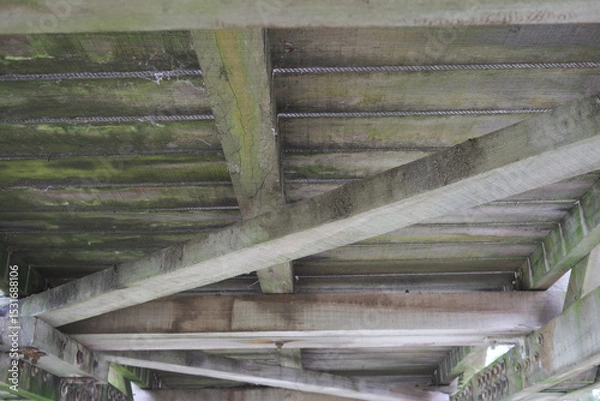 Fototapeta The wooden beams of a bridge are covered in moss and dirt
