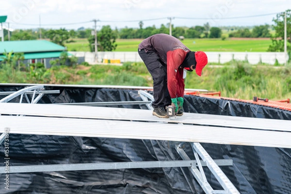 Fototapeta A worker is using a cordless screwdriver to remove screws from the metal sheet roof of the silo.