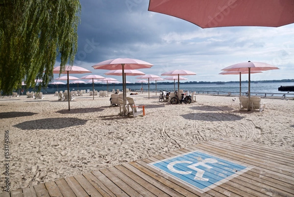 Fototapeta Wheelchair accessible rest area  for handicapped people on the public beach with the pink umbrellas