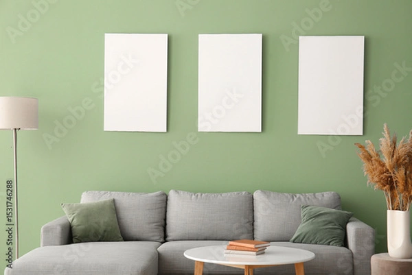 Fototapeta Comfortable sofa, table and blank posters on green wall in room