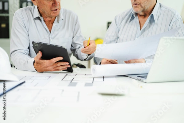 Fototapeta Two colleagues discussing data working and tablet, laptop with architectural project at construction site at desk